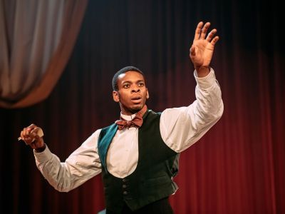 Actor in well dressed period costume of a white shirt and green waistcoat holding out his arms